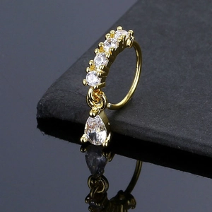Macro view of gold nose hoop with zircon stones and a teardrop pendant reflection