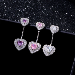 Vista macro di tre piercing all'ombelico a forma di cuore con zirconi viola e rosa