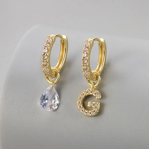 Macro detail van asymmetrische gouden oorbellen met traan-zirkonia en pavé-gezet letter G