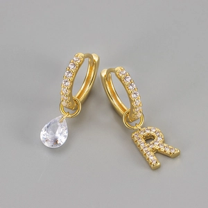 Detail van de asymmetrische gouden oorbel met peervormige zirkoon en hanger letter R
