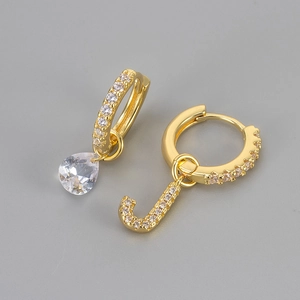 Detail van asymmetrische gouden letter J en waterdruppel zirkoon oorbellen met pavézetting