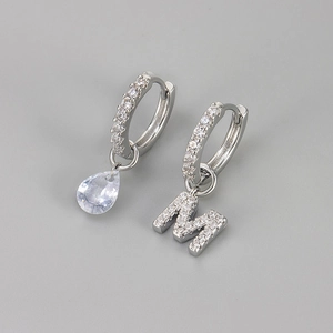Detail van asymmetrische oorbellen met waterdruppelsteen en ingelegde letter M-hanger