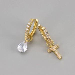 Detail van asymmetrische gouden oorbellen met kristallen druppel en letter T hanger