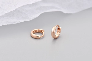 Dettaglio macro di orecchini huggie in oro rosa con finitura lucida e design minimalista