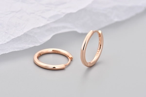 Dettaglio degli orecchini a cerchio oro rosa con marchio S925 su superficie metallica