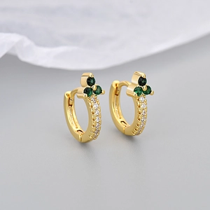 Macro detail of gold hoop earrings with green stones and sparkling white zircons