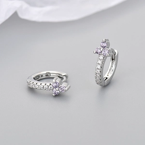 Close-up of silver earrings with purple floral zircons and white pave stones on gray
