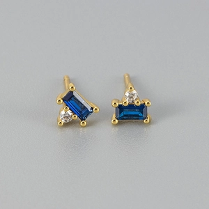 Detail of gold studs featuring rectangular blue gemstone and round white zircon
