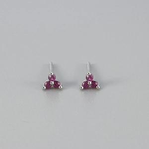 Detailopname van minimalistische zilveren oorknopjes met magenta zirkoon klavermotief