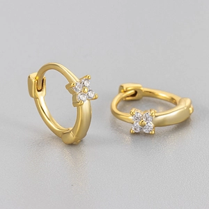 Macro detail of gold-plated clover huggie earrings featuring sparkling zircon inlay