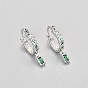 Detail of silver hoop earrings with emerald-cut green stone and star engravings