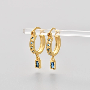 Detailed close-up of golden hoop earrings with blue zircon stones and engraved star patterns