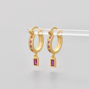 Detailed view of gold hoop earrings with starburst patterns and pink rectangular gemstones