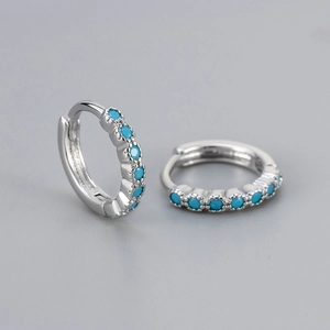 Macro detail of silver huggie earrings featuring turquoise stones and wave edge design