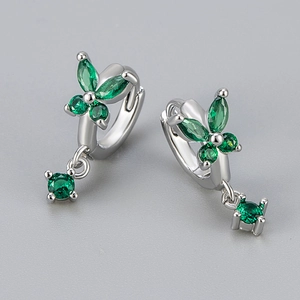 Macro shot of silver butterfly hoop earrings with emerald green zircons and floral pendants