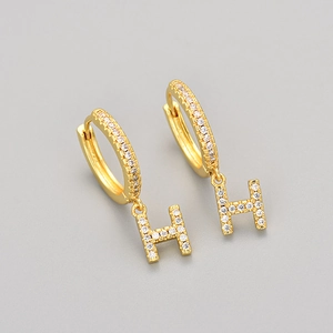 Detailed close-up of gold hoop earrings with crystal-encrusted letter H pendants