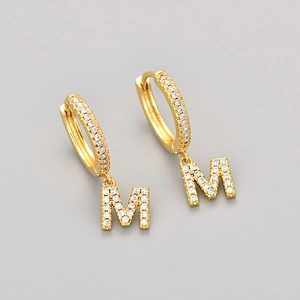 Close-up of golden hoop earring with letter M pendant and shimmering cubic zirconia stones