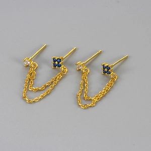 Detail of gold double piercing chain earring with white zircon and navy blue gemstones