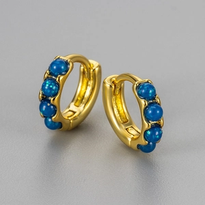 Macro detail of gold huggie earrings featuring inlaid round blue opal-like stones