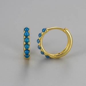 Detail of gold-plated hoop earrings featuring inlaid blue opal stones on a grey background