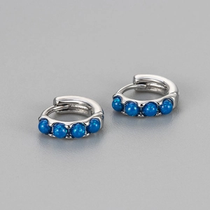 Macro shot of silver huggie earrings featuring four sparkling deep blue opal stones