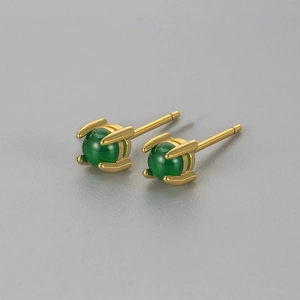 Orecchini a perno con zircone verde smeraldo dorati su una superficie grigia minimalista