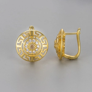 Detalle de pendientes dorados con diseño de greca griega y piedra color champán