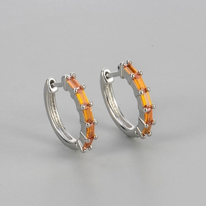 Close-up of silver huggie earrings featuring rectangular orange cubic zirconia stones