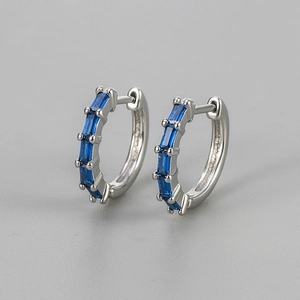 Detailed macro view of silver huggie earrings with baguette cut deep blue zircon stones