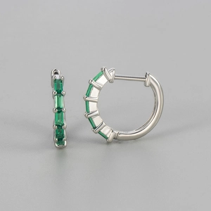 Close-up of silver hoop earrings featuring emerald green rectangular zircon gemstones