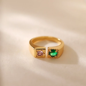 Dettaglio macro di anello aperto dorato con pietra a stella rosa e zircone verde