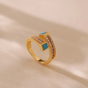 Dettaglio macro dell'anello dorato bypass con pietre turchesi quadrate e pavé di zirconi