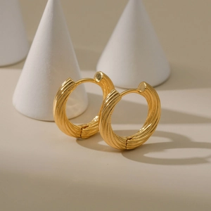 Elegante goldene Creolen mit spiralförmig gedrehter Textur auf geometrischen Requisiten