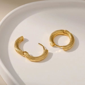 Minimalistische 18K vergoldete gedrehte Creolen auf einer weißen Porzellanschale