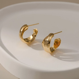 Elegantes pendientes de aro retorcidos bañados en oro de 18K sobre bandeja de cerámica
