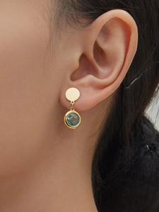 Detail of round green faceted stone earrings with gold plating worn by a model