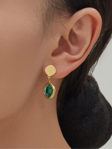 Close-up of geometric gold metal earrings with faceted green glass stones on a model