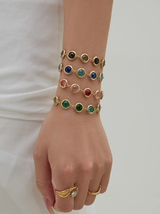 Close-up of elegant gold bracelets with colorful round stones on model wrist