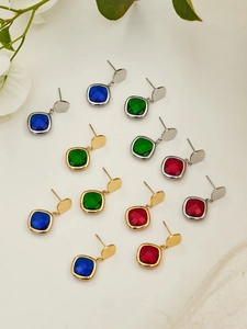 Detailed view of square cut gemstone earrings in blue, green, and red with gold metal finish