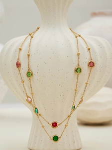 Detail of gold chain necklace with multi-colored faceted round gemstones on ceramic vase