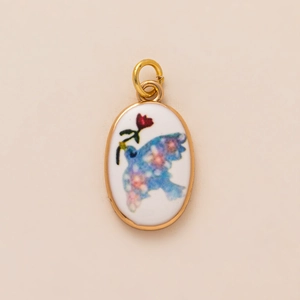 Detail shot of an oval gold pendant with a blue bird and red flower enamel design