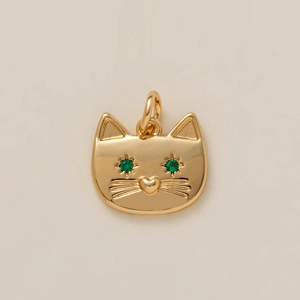Detailed macro view of a golden cat charm with vibrant green gemstone eyes and heart nose