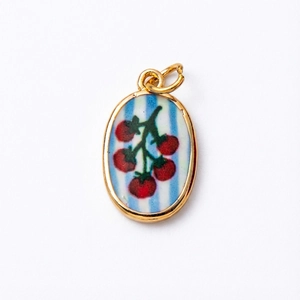 Détail d'un pendentif ovale plaqué or avec rayures bleues et motif de tomate rouge