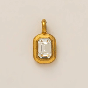 Macro detail of a gold-plated rectangular charm featuring a baguette-cut clear crystal stone