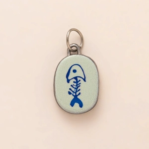 Detail of silver oval pendant with green enamel and blue fishbone motif on beige background