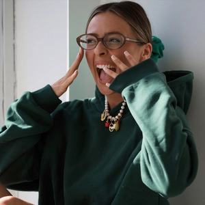 Detalle de sudadera verde oscuro con collar de perlas y colgantes de frutas y coches