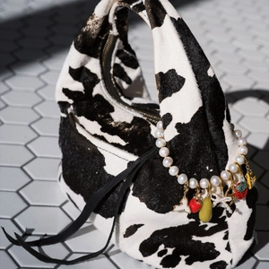 Detalle de bolso hobo con estampado de vaca y dijes de perlas con colgantes de fresa y pera