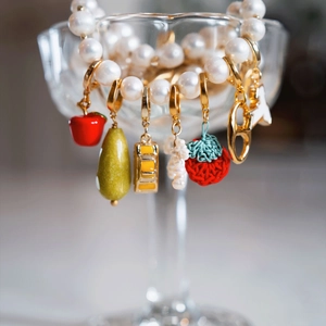 Detalle de joyería de perlas con dijes coloridos de manzana y fresa esmaltadas