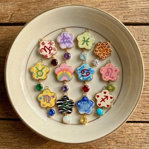 Pendentifs zodiaque fleur en or 18K avec breloques colorées sur plateau céramique
