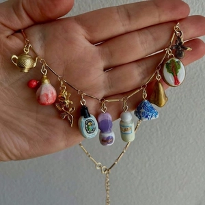 Hand hält eine goldene Edelstahlkette mit verschiedenen Miniatur-Kesselanhängern